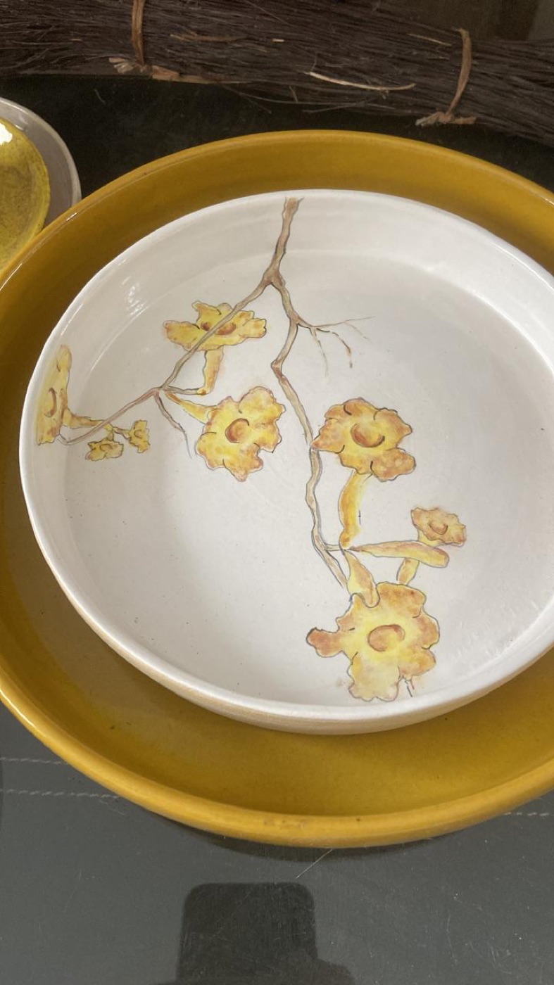 Tigela branca com ramo de flores amarelas, dentro de outra tigela dourada